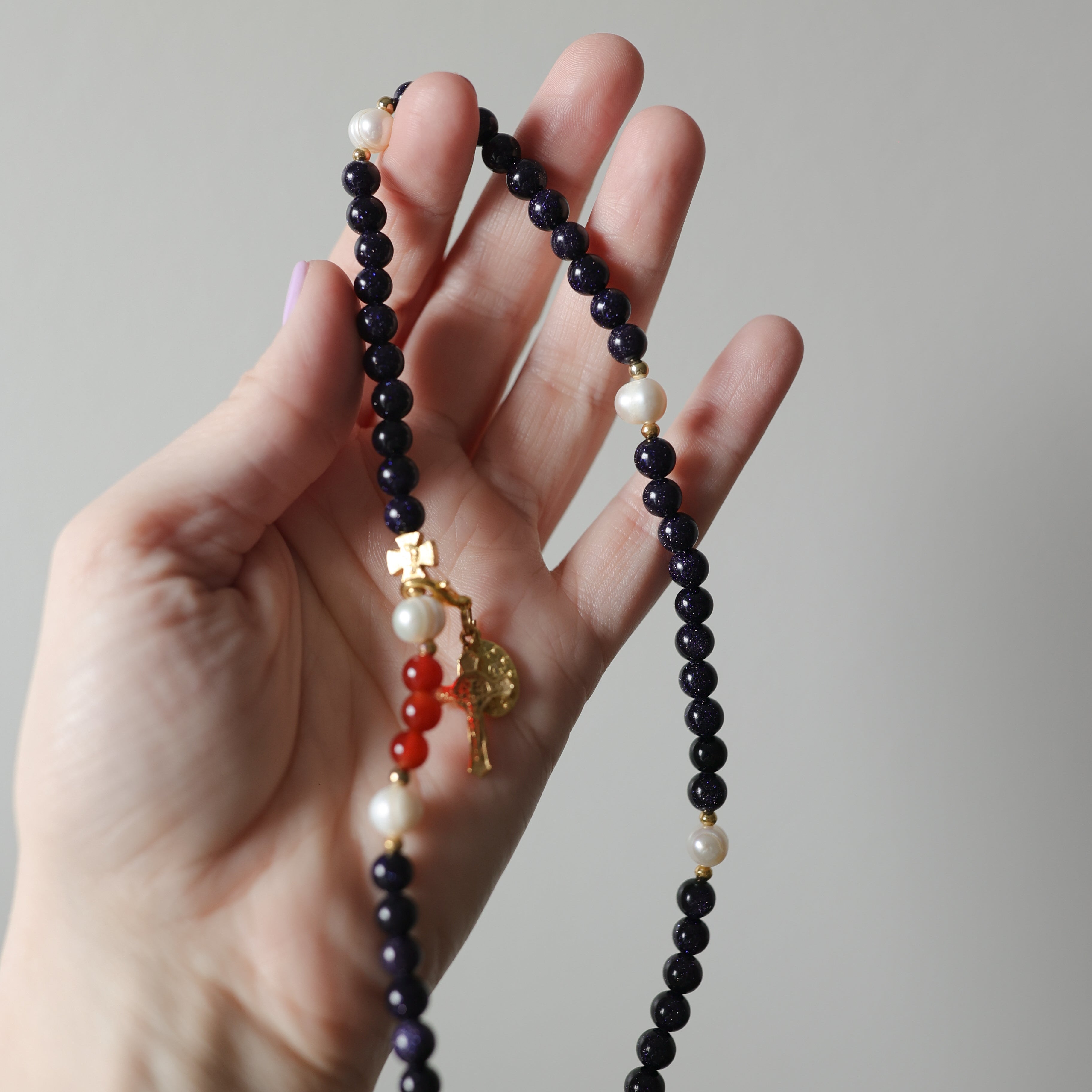 Hand holding a beaded rosary bracelet with various colored beads against a neutral background