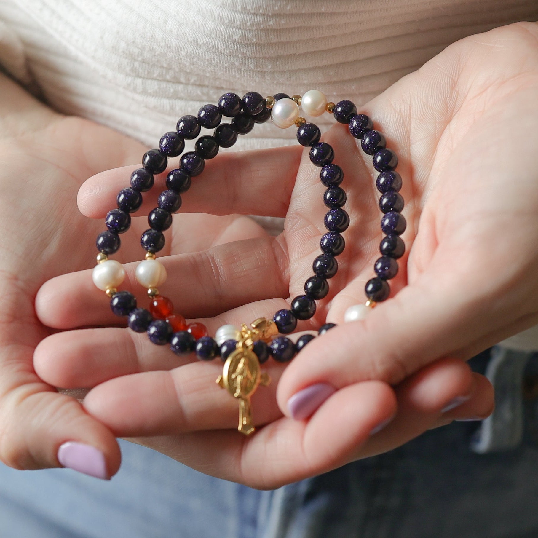 Hands holding a set of beaded bracelets with a neutral background