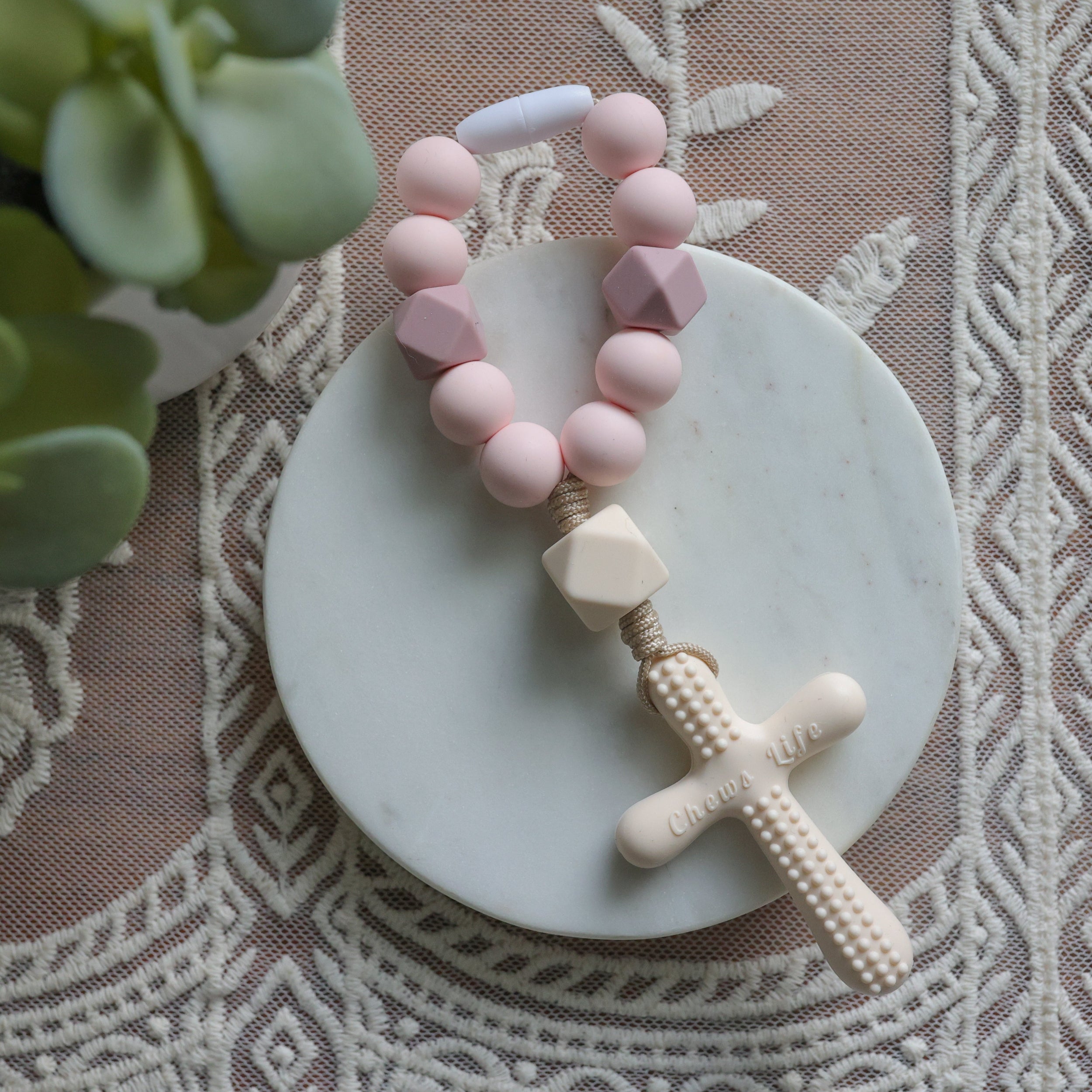 Pink and white baby teething necklace on a decorative plate with lace background