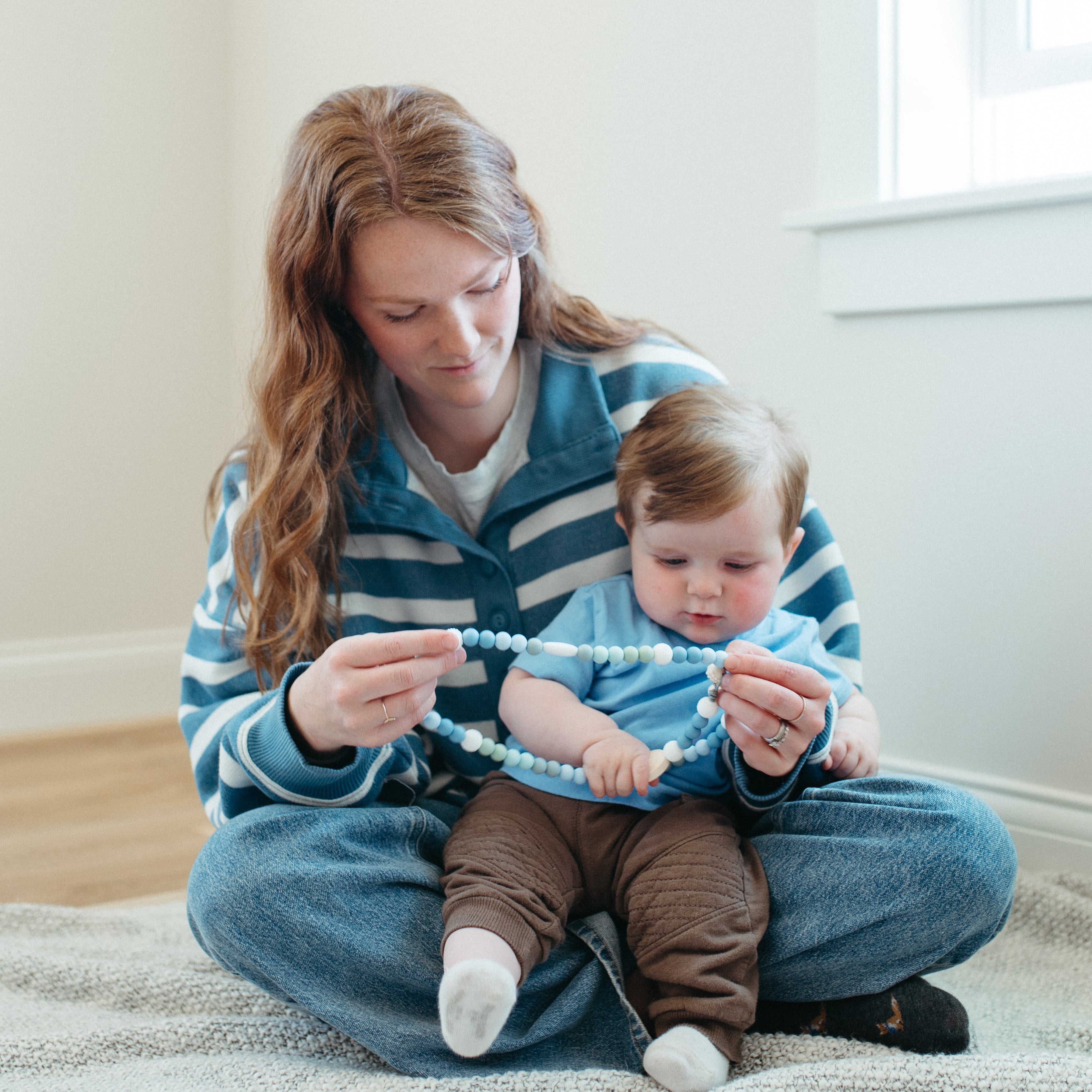 Woman sitting on the floor with a baby, both holding a silicone rosary together.
