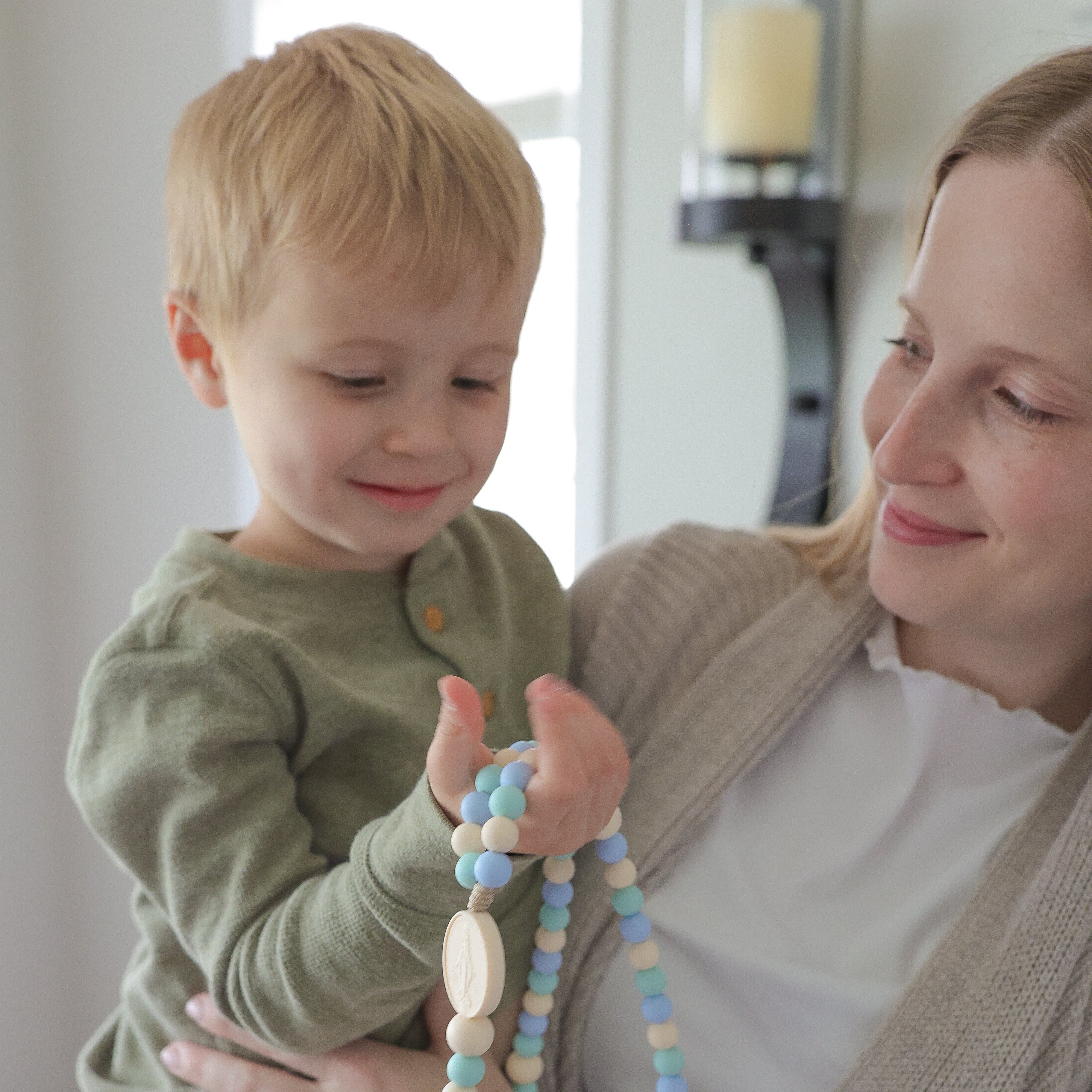 Woman holding a child and a necklace with beads in a home setting