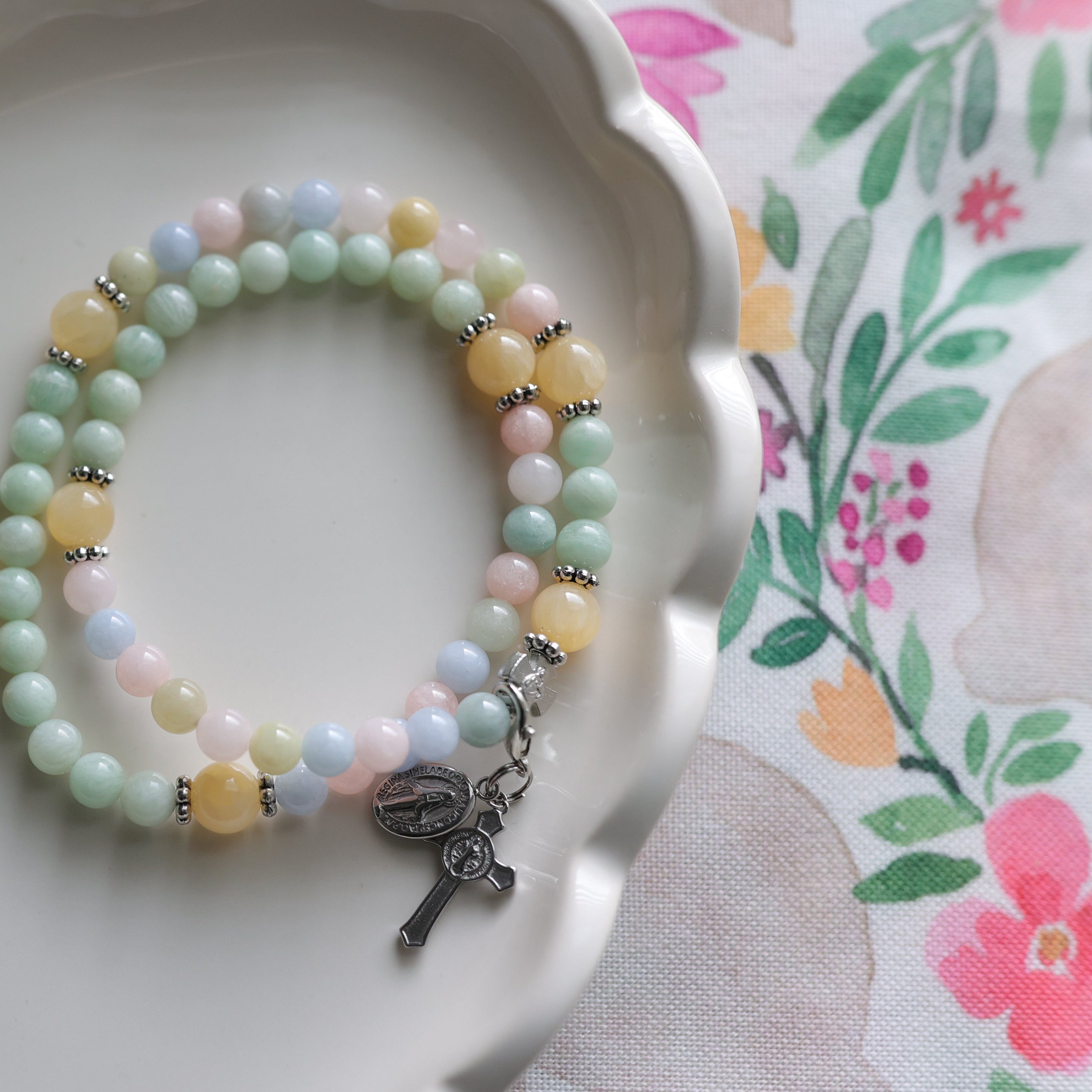 Double wrap rosary bracelets with cross charms on a decorative plate with floral background