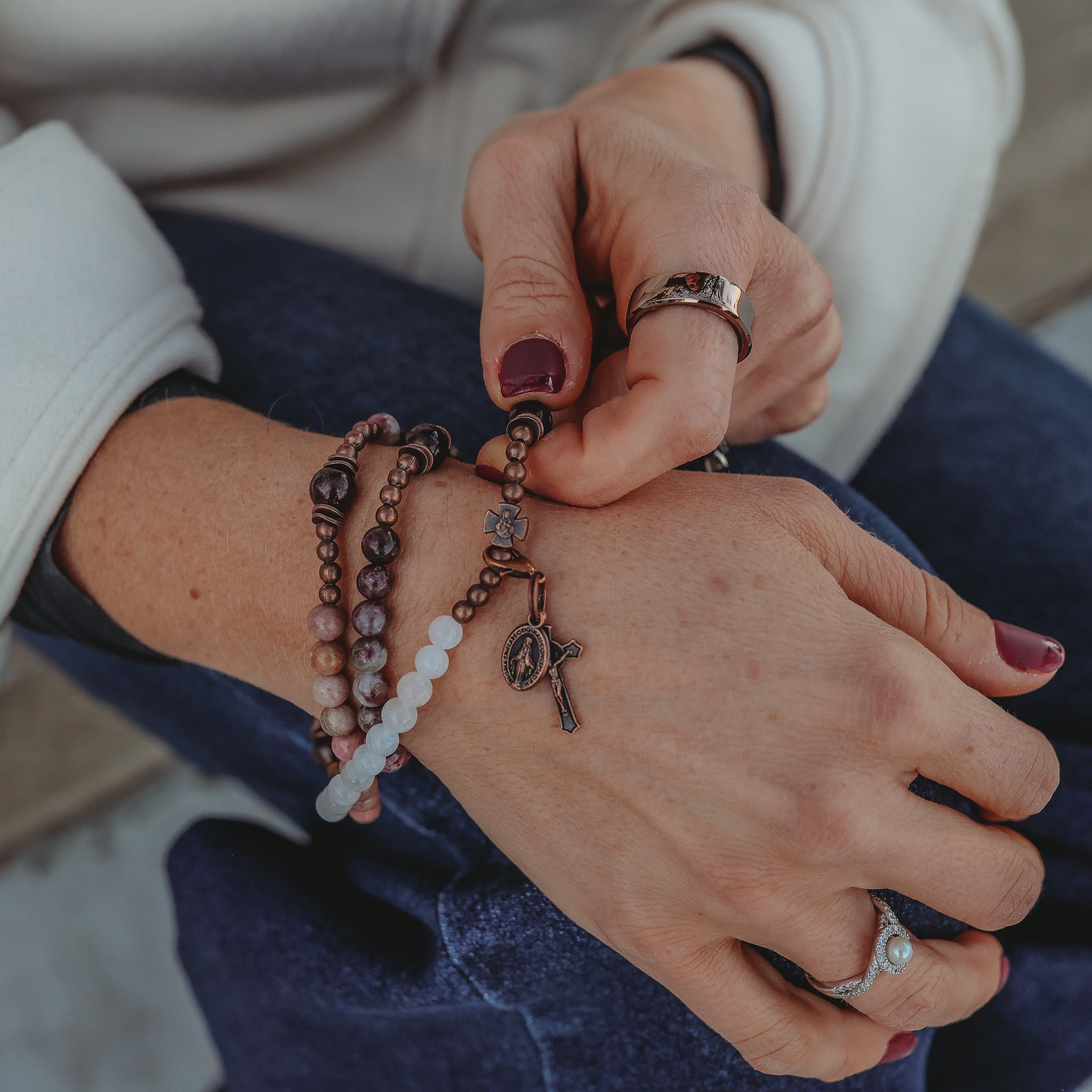 Close-up of hands wearing multiple bracelets and rings on a blurred background