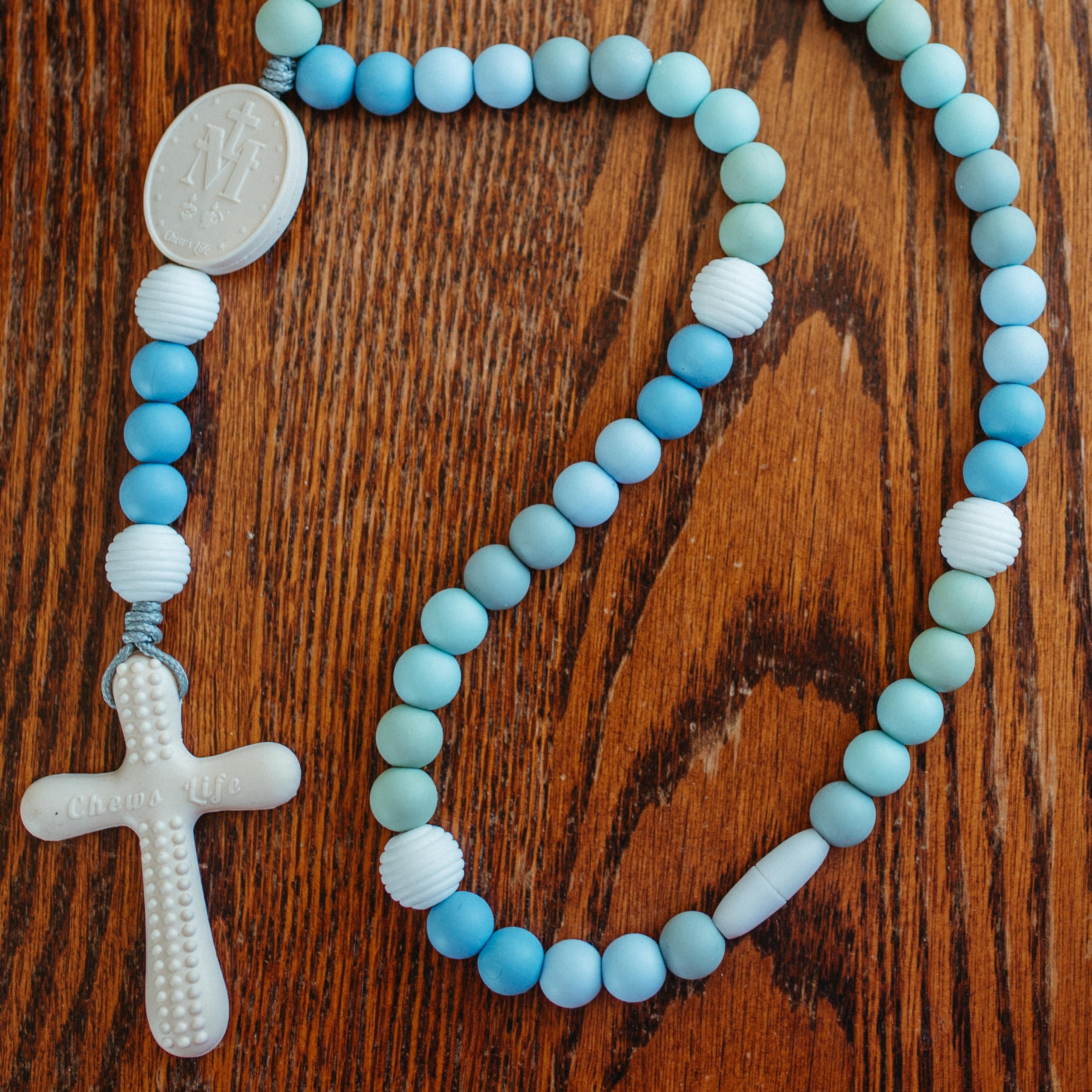 Blue and white silicone rosary for kids with a cross on a wooden surface