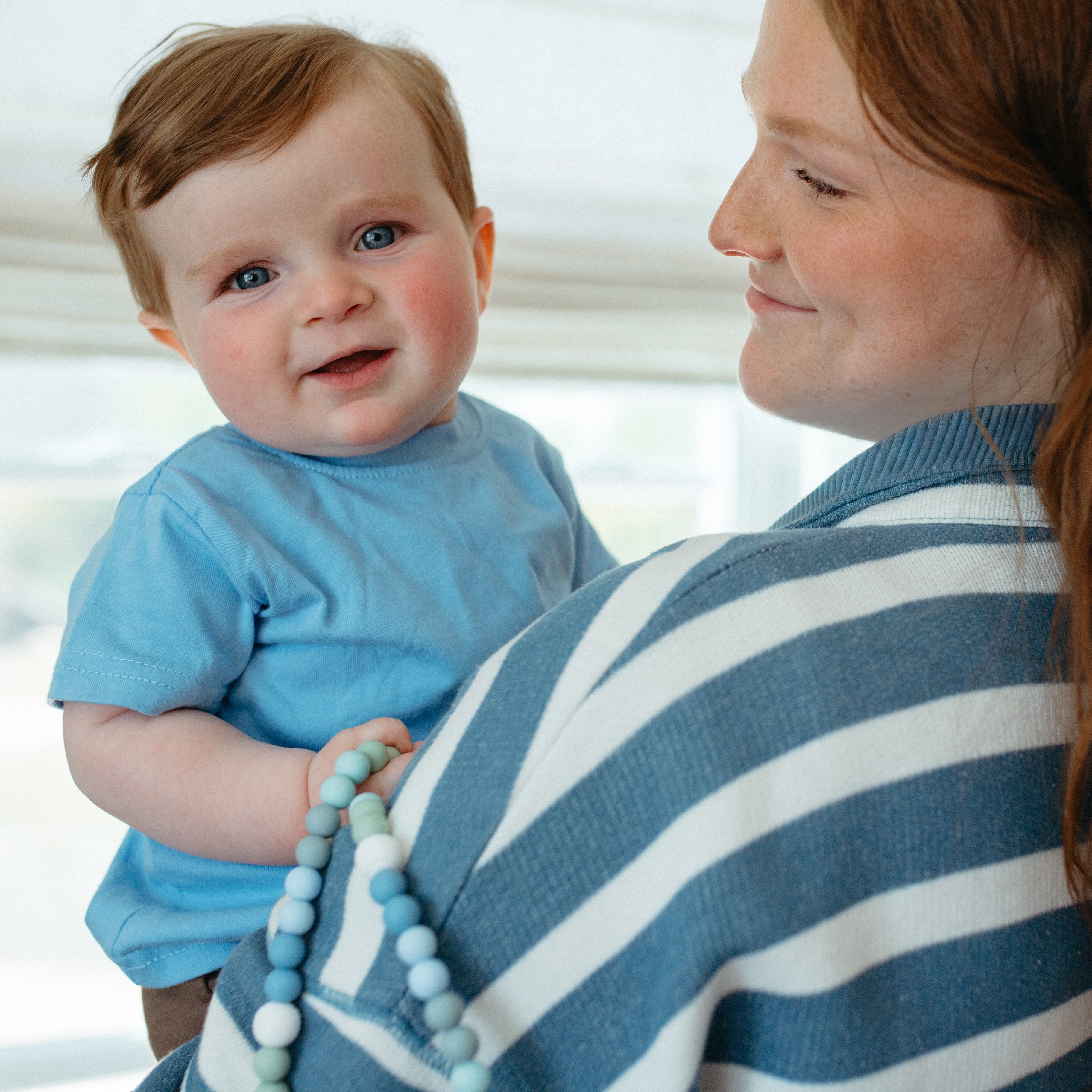 Woman holding a baby wearing a blue shirt indoors