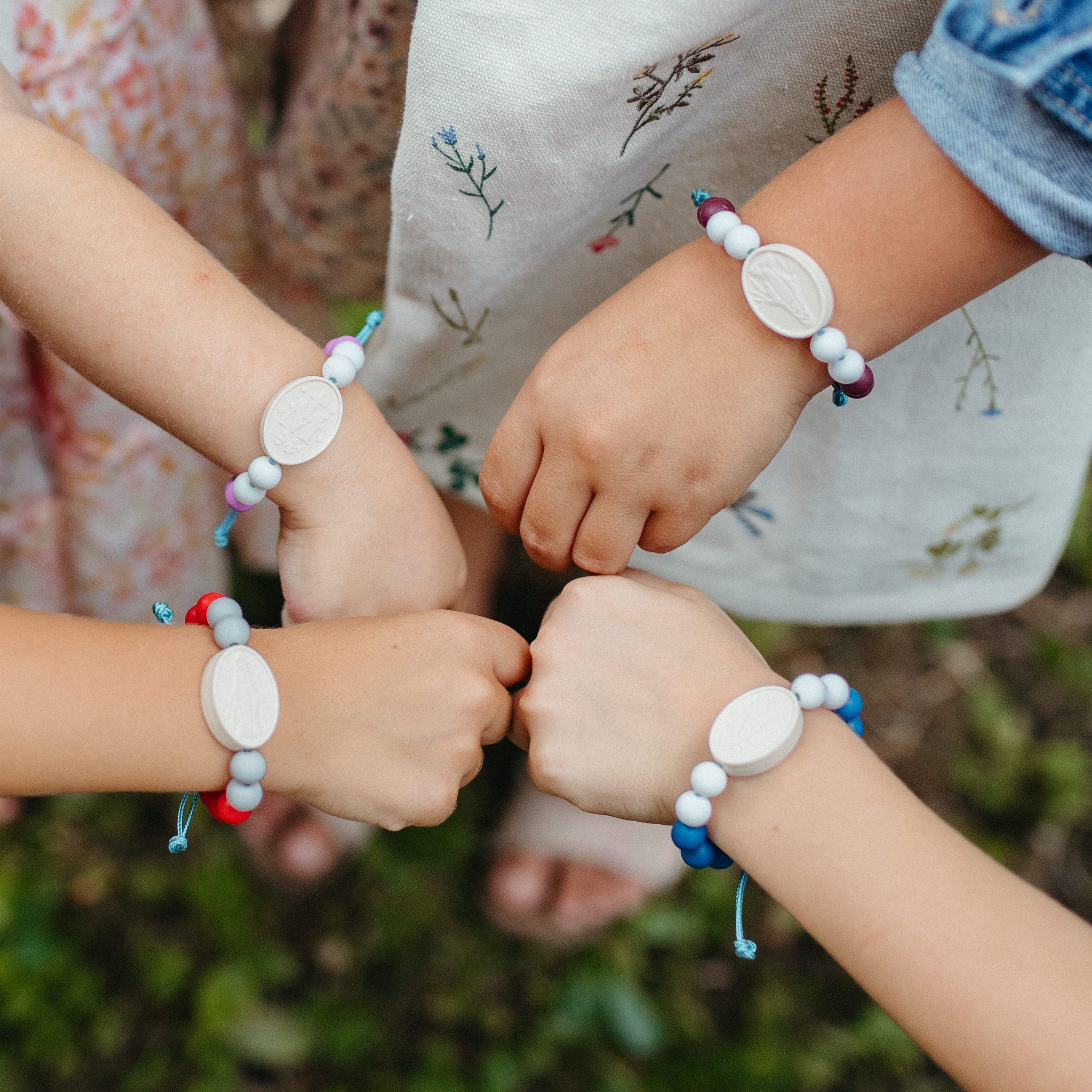 Four childrens wrist with silicone oval miraculous medal and silicone beaded bracelet in red, blue, purple or plum colors